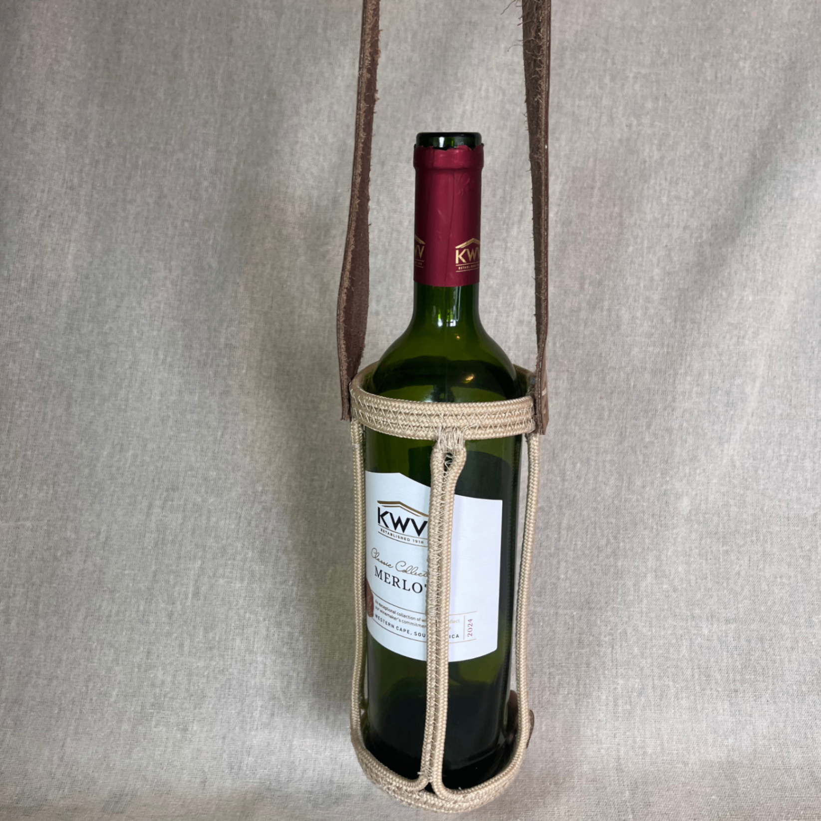 Rope wine carrier with a leather shoulder band holding a wine bottle